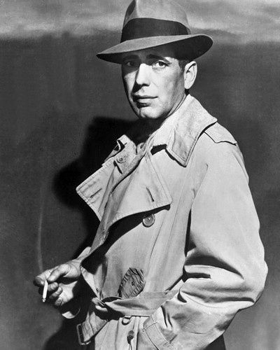 Humphrey Bogart was a famous Film Noir actor who starred in films such as 'The Maltese Falcon' (1941) and 'The Big Sleep' (1946). His characters represent the typical film noir anti-hero protagonist. He is seen here in a typical 1940s context; wearing a trilby hat, trench-coat and smoking. Rick Blaine, Bogie And Bacall, Bogart And Bacall, Noir Detective, Raincoat Outfit, Tom Selleck, Male Actors, Lauren Bacall, Humphrey Bogart