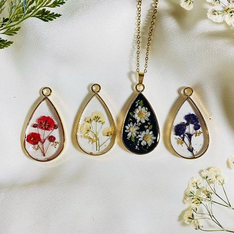 Discover the beauty of nature encapsulated in these stunning handmade botanical resin necklaces. Each teardrop pendant features real pressed flowers carefully preserved in resin, creating a one-of-a-kind piece that exudes elegance and charm. These resin jewelry pieces are perfect for nature lovers, boho fashion enthusiasts, and those who appreciate unique, artisan-crafted accessories. Available in various flower designs, including vibrant red, delicate white, and charming purple blooms, each necklace is a wearable work of art. The golden teardrop frame adds a touch of sophistication, making these pendants suitable for both casual and formal occasions. Whether as a thoughtful gift or a special addition to your jewelry collection, these floral necklaces are sure to impress. All of my jewelry Pressed Flower Jewelry Diy, Preserved Flower Jewelry, Resin Necklace Pendant, Pressed Flower Jewelry, Resin Flower Jewelry, Uv Resin Ideas, Adjustable Resin Jewelry With Pressed Flowers, Bohemian Jewelry With Pressed Flowers In Resin, Pressed Flowers Flower-shaped Jewelry Gift