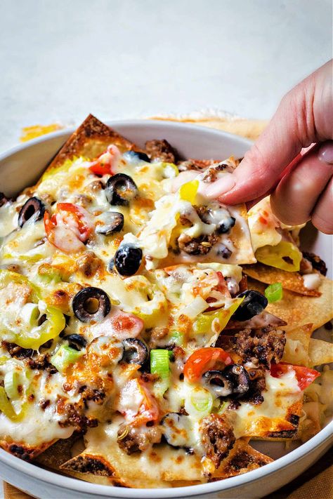 a hand picking up an Italian nacho from the pan. Different Types Of Nachos, Zios Italian Nachos Recipe, Italian Nachos Old Chicago, Johnny Carinos Italian Nachos Recipe, Wonton Nachos, Italian Nachos Recipe, Italian Nachos, Nachos Supreme Recipe, Nacho Appetizer