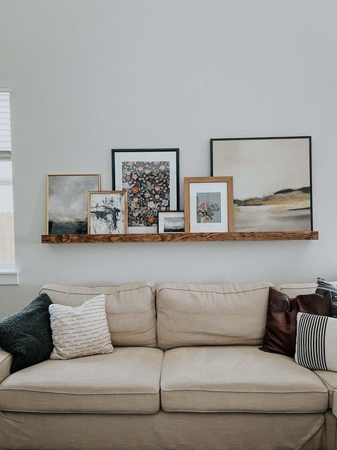 Above The Couch Photo Display, Floating Shelf With Photos, Above Couch Frame Layout, Photo Ledge Wall Living Rooms, Stacked Photos On Shelf, Leaning Photos On Shelf, Picture Ledge With Plants, Art Ledge Above Bed, Long Shelf With Pictures