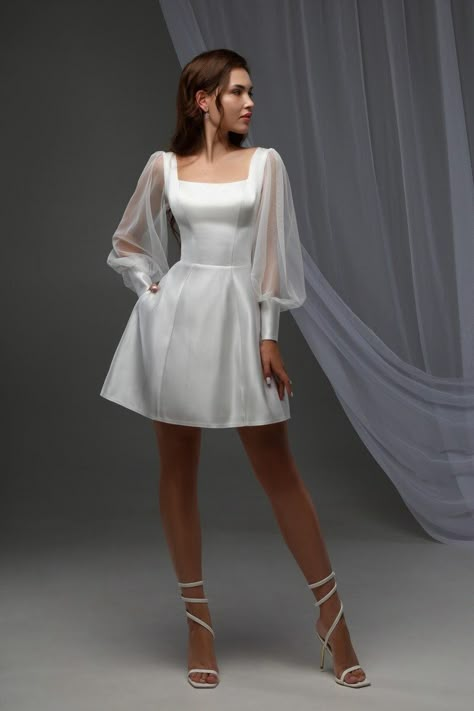 Dive into elegance with our Minimalist White Mini Dress, perfect for any cocktail event or special occasion! Its off-white satin fabric shimmers subtly, making you the center of attention.  - Square neckline & sheer lantern sleeves: A blend of sophistication and charm. - Corset top & natural waistline: Flaunts your figure while the mini length adds a playful twist.  - Pockets & lace-up back: Combine functionality with style. Ideal for summer weddings as a bridal mini dress or an engagement party White Wedding Cocktail Dress, White Bridal Cocktail Dress, Short Wedding Dress Retro, Cocktail Bridal Dress, Long Sleeve Mini Dress White, Mini Wedding Dress With Sleeves, Short White Vintage Dress, Skater Wedding Dress, Engagement Party Dress For Bride Casual