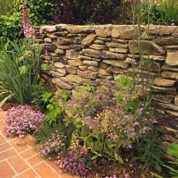 A dry-stacked stone wall looks so natural. The spaces between stones in the retaining wall allow water to drain through, relieving pressure. Another advantage of dry-stacked stone walls is that you can create planting pockets for small rock garden plants such as sedums. Garden Landscaping Design Ideas, Stone Walls Garden, Stacked Stone Walls, Gravel Landscaping, Rock Garden Plants, Rock Garden Design, Dry Stone Wall, Retaining Walls, Garden Landscape Design