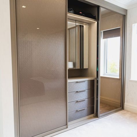 This decorative glass sliding door wardrobe opens to reveal a vanity unit with mirrors, LEDs and matching internal drawers. Neatsmith designs and installs bespoke wardrobes, dressing rooms and bedroom furniture to create your perfect bedroom. Our wardrobes are made to measure and are completely tailored to your needs. #walkinwardrobes #wardrobes #dressingrooms #home #bedroom #bedroomideas #bedroominteriors #madetomeasure Wardrobe Laminate Design With Mirror, Sliding Door Wardrobe Designs With Dressing Table, Dressing Unit In Wardrobe, Dressing In Almirah, Slide Almirah Design, Ladies Wardrobe Design Bedroom, Sliding Cupboard With Mirror, Glass Almirah Designs, Wardrobe Design Bedroom Sliding With Mirror