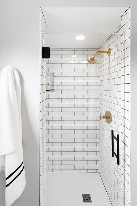 Behind a glass door fitted with an oil rubbed bronze handle, this gorgeous walk in shower boasts a white subway tile surround accented with gray grout, framing a tiled niche, and complementing a brass rain shower kit. Subway Tile Shower Designs, Gold Shower Head, White Subway Tile Shower, Shower Glass Door, Gray Grout, Subway Tile Showers, Black Floor Tiles, Grey Grout, Small Space Bathroom