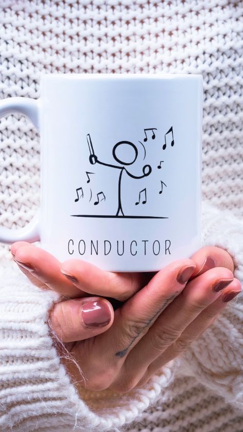 Una taza blanca de cerámica con el diseño minimalista de un director de orquesta (conductor) sobre las manos de una persona. Music