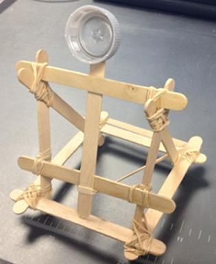 A photograph shows a small catapult structure made from Popsicle sticks, rubber bands and a plastic bottle cap. Catapult Medieval, Catapult Craft, Catapult Project, Catapult For Kids, Popsicle Stick Catapult, Plastic Bottle Caps, Maker Space, Bottle Cap Art, Bottle Cap Crafts