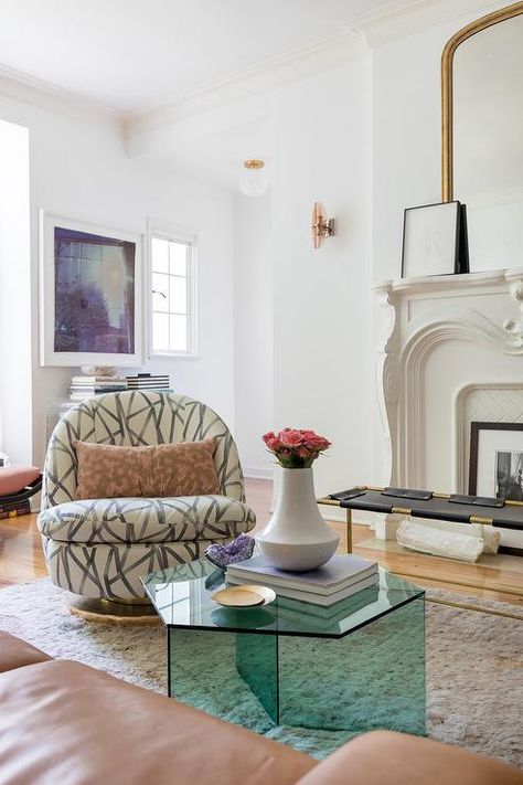 Luxurious living room features a brown leather sofa placed at a recycled glass hexagon coffee table positioned on a gray rug in front of a swivel chair finished with Kelly Wearstler Groundworks Channels' fabric while a gilt mirror sits atop a gorgeous white fireplace mantel. Old Hollywood Interior, Soho House Style, Fairy Office, California Minimalist, Old Hollywood Decor, White Fireplace Mantels, Japanese Room Decor, Hollywood Apartment, Hexagon Coffee Table