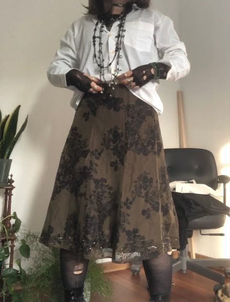 A mid-size person/girl wearing a closed wide white button up with a black ripped tights longsleeve under it, a dark green flower midi skirt, rose patterned stockings,  black platform dr. Martens and multiple crystal rings and bracelets. 	The person is also wearing multiple silver necklaces; one in form of a moon, a butterfly, and one in form of a fairy, a long black and green bead necklace and a green buttery choker. Cottagecore Pirate Aesthetic, Sparkly Clothes Aesthetic, Pirate Academia Aesthetic, Goblincore Skirts, Moss Aesthetic Outfit, Crystals Aesthetic Outfit, Masc Skirt Outfit, Pirate Cottagecore, Earth Goth