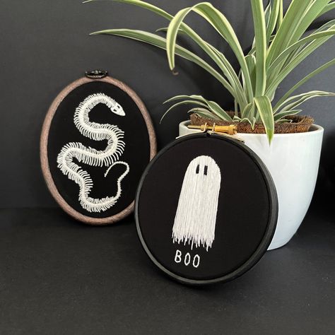 Two embroidery hoops - one a snake skeleton in white on black fabric in a wood style plastic hoop and one with a ghost in white with ‘boo’ written underneath it on black fabric in a black hoop. They are propped up against a spider plant. Snake Skeleton Embroidery, Goth Embroidery Clothes, Trash Pants, Goth Sewing, Spooky Sewing, Witchy Embroidery, Goth Embroidery, Gothic Embroidery, Tattoo Room