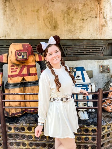 I’m wearing a white long sleeve knee length dress and a silver belt to represent Princess Leia in Disney Worlds Galaxy’s Edge. I topped off the look with my Mickey ears that have brown yarn on them to look like Princess Leia’s space buns and my actual hair is in two braids. I’m standing in front of two Droids to add to the Star Wars effect. Princess Leia Disney Outfit, Disney Galaxy Edge, Princess Leia Disneybound, Princess Leia Inspired Outfit, Starwars Disney Outfit, Princess Leia Disney Bound, Disney Star Wars Outfit, Disney Bound Outfits Star Wars, Princess Leia Outfits