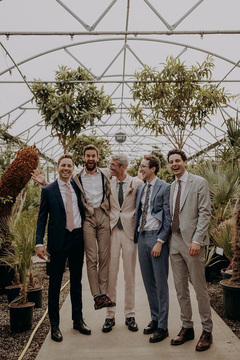 Groomsmen pose for photo in tonal neutral suits surrounded by plants Groomsmen Attire Mix And Match, Groomsmen Casual Wedding, Mixed Groomsmen Attire, Different Color Suits Groomsmen, Multicolor Groomsmen Attire, Mismatched Suits Wedding, Mix Matched Groomsmen, Formal Garden Party Attire Men, Groomsmen Ties Mismatched