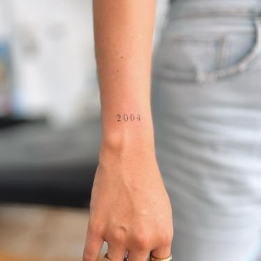 Commemorate a significant year with a small '2004' tattoo inked on your outer wrist. This ink serves as a timeless tribute to cherished memories. Follow us for more tattoo inspiration and ideas! #OuterWristTattoo #MemorableYear #NumericalInk #TattooInspiration Tattoo image credit - @pollytatttoo Explore a variety of tattoo styles, trends, and meanings on our website! Tattoo On Outer Wrist, Meaningful Wrist Tattoos For Women, Lower Back Tattoo Ideas, Inner Wrist Tattoos, Lower Back Tattoo, Side Wrist Tattoos, Meaningful Wrist Tattoos, Back Tattoo Ideas, Tribute Tattoos