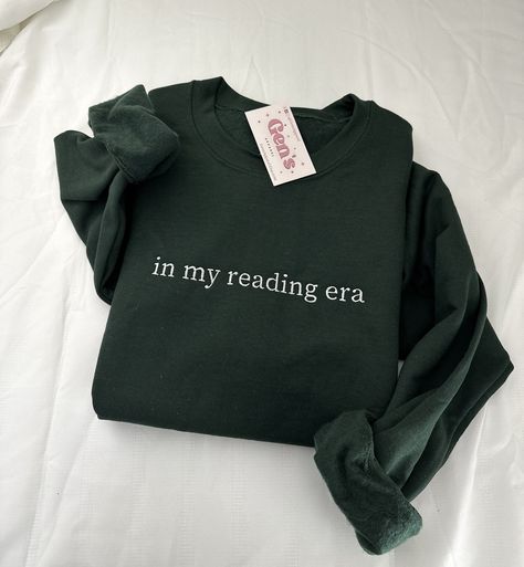 Step into your reading era with our "In My Reading Era" embroidered sweatshirt, a must-have for every book lover. This minimalist book sweatshirt, a perfect book club gift, effortlessly combines comfort and literary style, ensuring you join the exclusive ranks of the Reading Crew with unparalleled flair. Color in example is  Forest Green * 50% cotton, 50% polyester * Pre-shrunk * Classic fit * 1x1 athletic rib knit collar with spandex * Air-jet spun yarn with a soft feel and reduced pilling * Do Bookish Cotton Sweatshirt With Letter Print, Cotton Letter Print Bookish Sweatshirt, Literary Long Sleeve Cotton Tops, Reading Era, Minimalist Book, Bookclub Gifts, Lover Sweatshirt, Book Clothes, Embroidered Sweatshirt