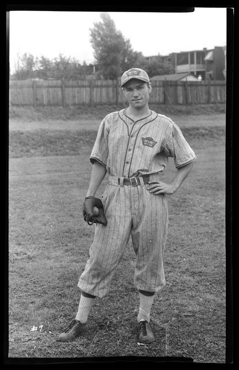 Vertical, black and white photograph of an exterior view depicting a man wearing a baseball uniform and a catcher's mitt on his right hand. He holds a baseball in the mitt, and his other hand is on his hip. There is a field, wooden fence, and houses visible in the distance. Old Baseball Photos, Vintage Baseball Uniforms, Sports Product Photography, 1900s Pictures, Vintage Baseball Aesthetic, 1950s Baseball, Baseball Poses, Organized Ideas, Baseball Clothes