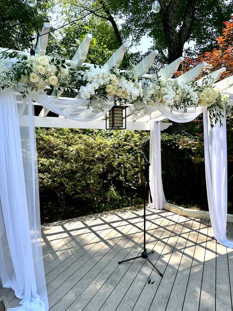 White garden arbor draped with white sheer fabrics and white flowers such as phalaenopsis orchids, white roses, baby’s breath, hydrangea. White Pergola Wedding, Pergola Wedding Decorations, Orchid Centerpieces Wedding, Wedding Ceremony Decoration, Orchids White, White Pergola, Arbor Wedding, Orchid Centerpieces, White Drapes