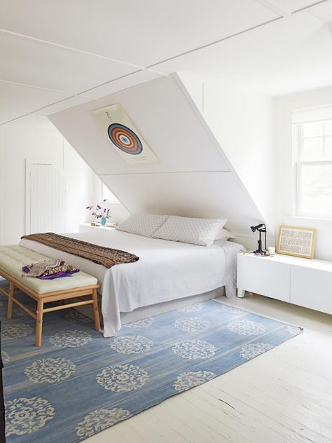 This master bedroom relies on a bright white color scheme, minimalist design and a sharp, sloped ceiling for its clean, crisp look. A blue patterned rug adds a dash of color and texture to the space. Slanted Ceiling Bedroom Ideas, Bedroom Ideas Slanted Ceiling, Sloped Ceiling Bedroom Ideas, Slanted Ceiling Bedroom, Sloped Ceiling Bedroom, Low Ceiling Bedroom, Small Attic Bedroom, Slanted Walls, Slanted Ceiling