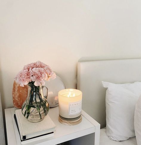 A white bedside table with a candle, salt lamp, pink flowers, and a stack of books. Bedside Table White, Lamp Candle, Room Decoration Ideas, Candle Table Decorations, Aesthetic Clean, Bedroom Oasis, Bedroom White, Bedroom Decorations, Himalayan Salt Lamp