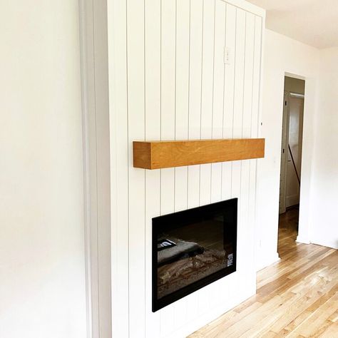 Fireplace surround in Lincoln, NE, featuring vertical shiplap painted white, black electric fireplace, and custom wood mantle in honey-colored stain. Vertical Shiplap Mantle, Shiplap On Sides Of Fireplace, Vertical Panel Fireplace, Shiplap Vertical Fireplace, White Wood Panel Fireplace Wall, Vertical Paneling Fireplace, Vertical Boards On Fireplace, Diy Vertical Shiplap Fireplace, Vertical Shiplap On Fireplace