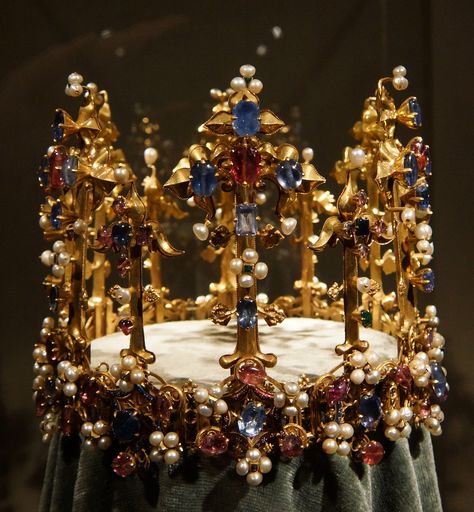 Earliest recorded medieval crown, first recorded in a list of 1399. Anne of Bohemia. It has twelve (Fleur de Lys) lilies rising from the circlet, alternately tall and short. The circlet's design is based on twelve gold rings beneath the lilies, mounted with hexagonal shapes in alternating red and blue enamel and gold openwork elements, underneath the circlet. All 12 stems are removable and numbered for correct placement Bohemian Crown, Crowns Royal, Medieval Crown, Royal Jewellery, Richard Ii, Ancient Jewels, Royal Crowns, Royal Tiaras, Crowns And Tiaras