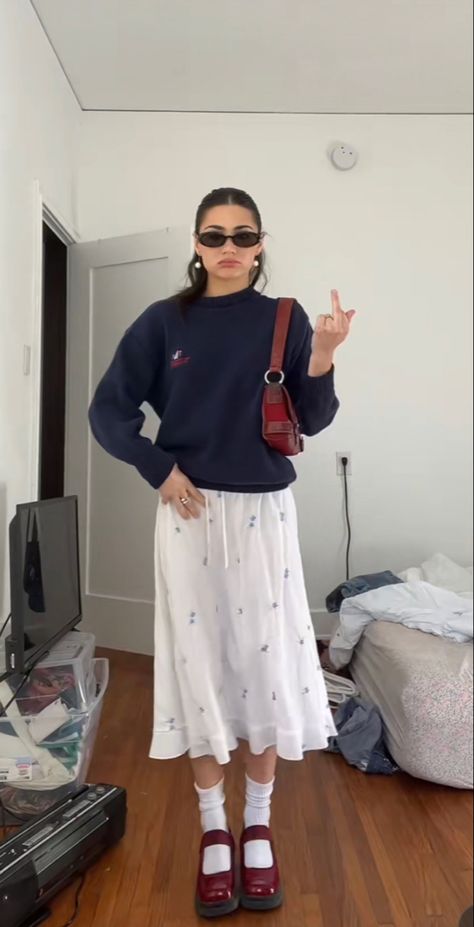 blue pullover, long flowy white skirt with flower print, red statement bag, and red marry janes