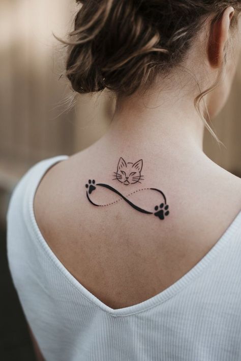 This tattoo features a simple cat face with an infinity symbol, accented by small paw prints.Positioned on the upper back, it represents eternal love and connection.The minimalist design keeps it clean and symbolic, perfect for someone wanting a quiet, meaningful tribute to their cherished pet. Cat Memorial Tattoos, Cat Memorial Tattoo, Cat And Dog Tattoo, Memorial Tattoo Ideas, Cat Tattoo Simple, Animal Symbolism, Memorial Tattoo, Memorial Tattoos, Wolf Tattoos