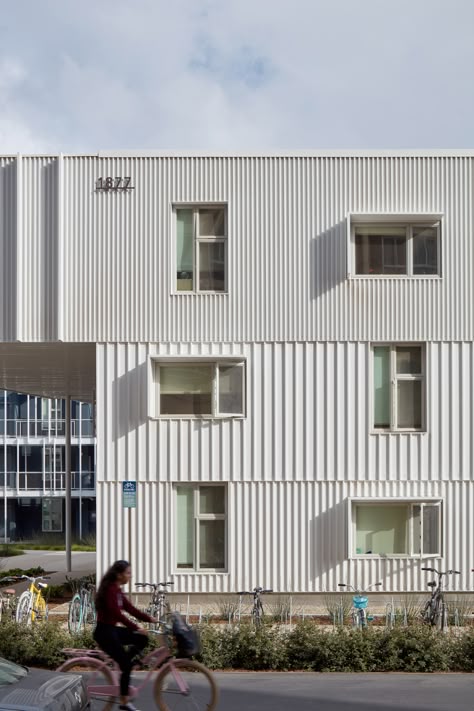 LOHA's San Joaquin Student Housing For the perimeter elevations, the team used white, corrugated metal cladding that evokes shipping containers. The courtyard-facing walls are sheathed in grey plaster.  White-painted steel was used for the outdoor staircases and corridors. Aluminium fins frame the corridors, helping reduce sun exposure. Multifamily Architecture, Metal Facade, Passive Design, Metal Cladding, Creative Architecture, Student Housing, Student House, White Building, Building Facade