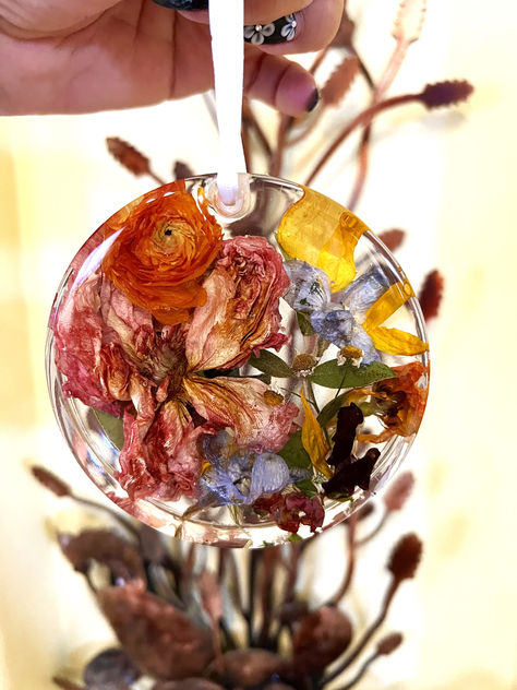 Close-up of a 4-inch round epoxy resin ornament showcasing vibrant fall wedding bouquet flowers in shades of red, orange, yellow, and blue, preserved as a timeless keepsake with a white ribbon for hanging. Preserving Wedding Flowers, Vibrant Fall Wedding, Flowers In Epoxy Resin, Green Valley Arizona, Flowers In Epoxy, Resin Keepsake, Wedding Flower Preservation, Fall Wedding Bouquet, Wedding Bouquet Preservation