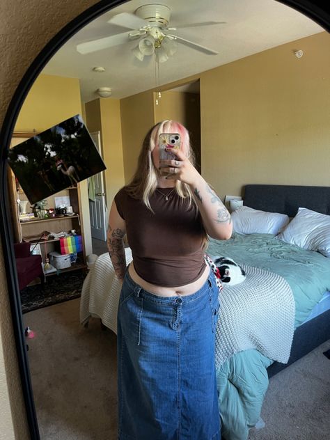 Girl standing in her room infront of a mirror with a brown baby tee crop top on and dark denim low waisted skirt with red threaded details around the button. The skirt almost looks cargo like. She's around midsize to fat and wearing a necklace. There's a cat behind her on a bed and the picture is taken in a bedroom. Crop Tops Mid Size, Mid Size Crop Top Outfit, Fat People Outfits, Baby Tee Outfit, Low Rise Skirt, Long Skirt Summer, Brown Crop Top, Low Waist Jeans, Dazzling Dress