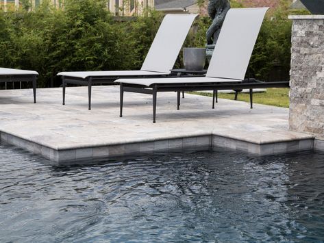 A dark finish, silver travertine deck and sleek loungers give this pool a modern feel. NPT Waterfall Yosemite’s gentle streaks and contemporary gray stone-like appearance make it the perfect waterline tile choice.  Call 888.476.POOL to find supplies and service professionals in your area. Travertine Pool Decking, Travertine Deck, Waterline Pool Tile, Waterline Tile, Swimming Pool Renovation, Silver Travertine, Travertine Pool Coping, Geometric Pool, Travertine Pool