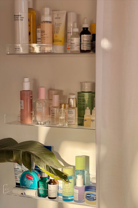 A set of clear acrylic shelves mounted on a wall, displaying an array of skincare products in a neat and organized manner. The shelves hold various serums, lotions, and creams, highlighting the beauty of clear storage solutions. Skincare Wall Shelf, Kids Book Display, Book Display Shelves, Skincare Display, Organization Skincare, Skincare Shelf, Clear Shelves, Acrylic Shelves, Book Display Shelf