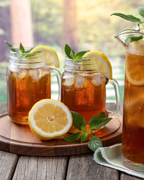 Pitcher of cold iced tea with mint, lemon slices and ice with two glasses ot tea on a wooden table and rural summer background Iced Tea Aesthetic, Ice Lemon Tea, Iced Tea Maker, Tea Aesthetic, Lemon Slices, Simply Filling, Tea Maker, Glass Carafe, Tea Makers