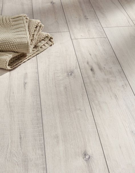 Gala Oak White takes inspiration from natural oak and reproduces its organic charm accurately with rustic grain patterns, a textured surface and 4-sided V-groove planks. A convenient and more affordable alternative to solid wood flooring, this laminate floor is designed to handle the pressures of heavy foot traffic anywhere, from family homes to busy commercial spaces. The 12mm thick planks measure 188mm in width, making them perfect for medium-sized and larger rooms. Easy to clean and to mainta White Wood Laminate Flooring, White Laminate Flooring, White Wooden Floor, Beach House Flooring, Direct Wood Flooring, Coastal Flooring, White Wood Floors, Residential Flooring, Oak Laminate Flooring