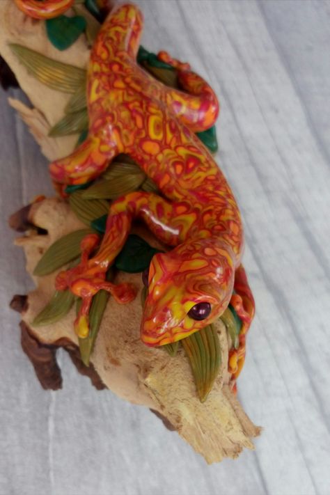 Image shows a handmade gecko sculpture made from polymer clay in shades of red, orange and yellow, with an intricate pattern over the surface. The gecko is mounted on a piece of driftwood with sculpted leaves. Gecko Clay Sculpture, Polymer Clay Gecko, Clay Salamander, Ceramic Gecko, Gecko Sculpture, Clay Gecko, Modeling Clay, Orange And Yellow, Clay Sculpture