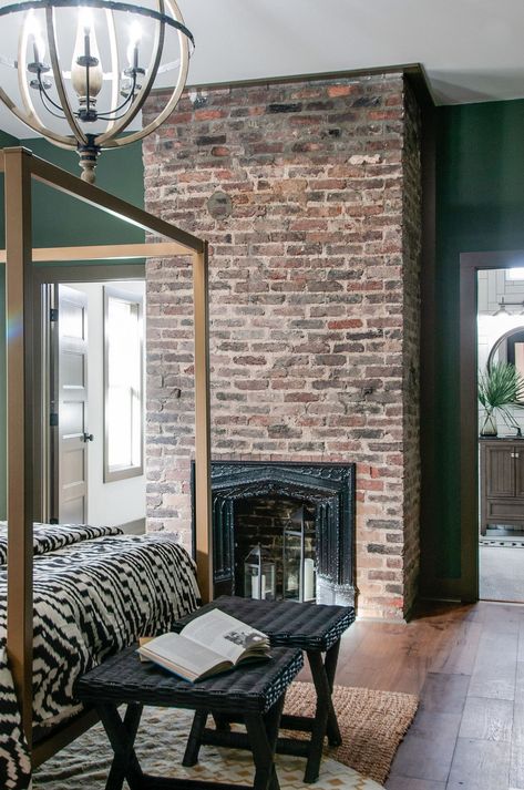 The original brick fireplace gives this green master bedroom so much character! Red Brick Fireplace Colors That Go With, Brick And Green Wall, Green Living Room Brick Fireplace, Brick And Green Interior, Accent Wall With Brick Fireplace, Green Walls With Brick Accent Wall, Exposed Brick Fireplace Bedroom, Brick Stain Interior, Exposed Brick Chimney Living Rooms