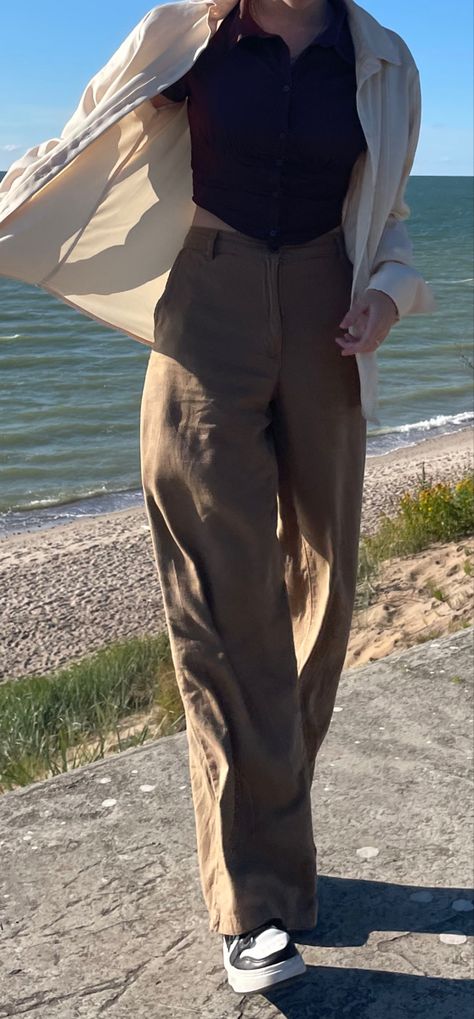 Woman standing by the sea. windy, flowy clothing, beige colors. Asymmetric corset top, wide-end pants. Blue/ brown color palette/light setting Old Fashion Summer Outfits, Dark Academia 90s Aesthetic, Outfit Ideas Old School, Dark Academia Outfit Inspo Summer, Summer Fits Dark Academia, Dark Academia Travel Outfits, Summer Outfit Academia, Modern Light Academia Outfits, Old Clothing Aesthetic