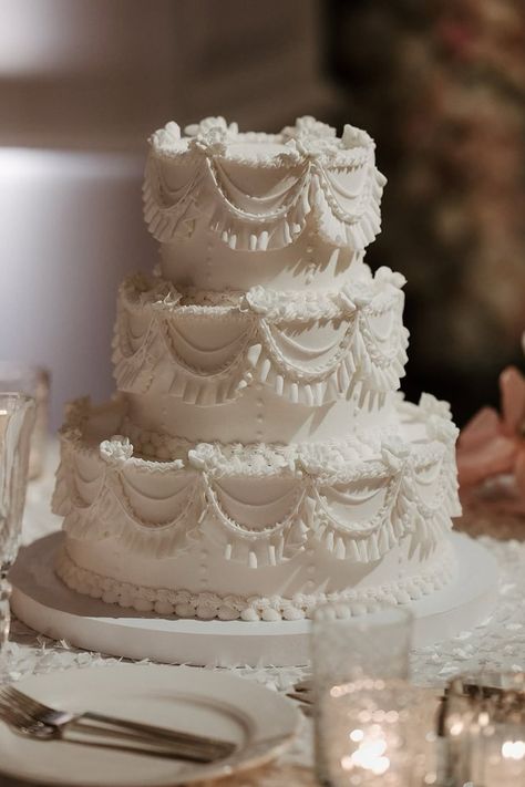 This white vintage 3-tier wedding cake is a stunning blend of classic elegance and intricate detail.  The delicate piping work, cascading swags, and lace-like textures give it a timeless, retro feel, making it a perfect centerpiece for a vintage or traditional wedding.  The all-white design exudes sophistication, making it an ideal choice for winter weddings, where it pairs beautifully with candlelit receptions, snowy backdrops, and elegant décor.  The intricate detailing adds depth and texture, creating a show-stopping cake that feels both luxurious and nostalgic.  Whether you're drawn to old-fashioned charm or simply love elegant wedding cakes, this design is a gorgeous inspiration. Cake design by fancy cakes by lauren - Photo by parker grey photo Fancy Tiered Cakes, Vintage Piping Wedding Cake, Old School Wedding Cakes, Classic Wedding Cake Vintage, Victorian Cake Design, Baroque Wedding Cake, Victorian Wedding Cakes, Wedding Cake Designs Elegant, Christmas Wedding Centerpieces