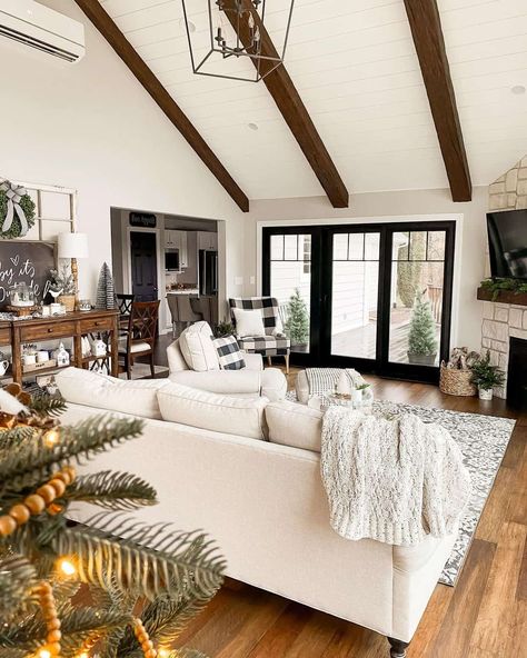 Black framed French door flanked by matching black windows are positioned underneath a white sloped shiplap ceiling with dark wood beams. An ivory couch adorned with an off-white knit throw blanket faces the door. White Vaulted Ceiling, Vaulted Ceiling With Wood Beams, Ceiling Beam Ideas, Ceilings With Wood Beams, Dark Wood Beams, Ceilings With Wood, Ivory Couch, Ceiling With Wood, Beam Ideas