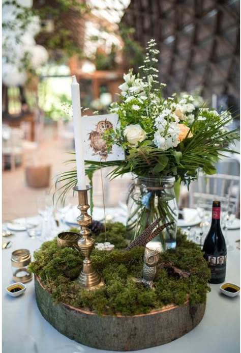 a woodland wedding centerpiece of a wood slice, moss, blooms and greenery in a jar, feathers and candles Boho Chic Forest Wedding, Woodland Fairy Wedding Table Decor, Nature Themed Table Decor, Moss Decorations Wedding, Moss Table Wedding, Enchanted Woodland Wedding, Woodland Wedding Table Decor, Woodland Table Centerpieces, Moss And Blush Wedding