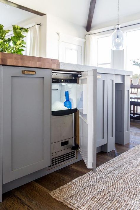 A stainless steel ice maker is concealed behind a cabinet door of a gray blue kitchen island accented with antique brass cup pulls and butcher block top and white quartz countertop. Built In Icemaker In Kitchen, Icemaker In Kitchen Island, Undercounter Ice Maker, Ice Drawer, Sink Dishwasher, Grey Blue Kitchen, Blue Kitchen Island, Freezer Drawer, Drink Fridge