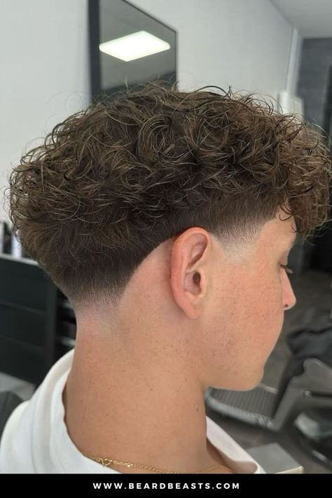 A close-up image of a stylish curly taper fade haircut. The hair on top features soft, voluminous curls, gradually tapering down to a clean fade at the sides and back of the head. This curly taper fade offers a sharp contrast between the thick curly texture and the neatly faded sides, making it a popular and modern choice for those with curly hair looking for a fresh, low-maintenance style. Ideal for enhancing natural curls while keeping the sides sleek and neat. Mid Taper Fade Wavy Hair, Low Taper Burst Fade, Low Taper Fluffy Hair, Fades For Curly Hair, Low Taper Curly Hair Men, Drop Fade Curly Hair, Taper Fade Haircut Curly Hair, Taper Curly Hair, Low Taper Fade Haircut Curly Hair