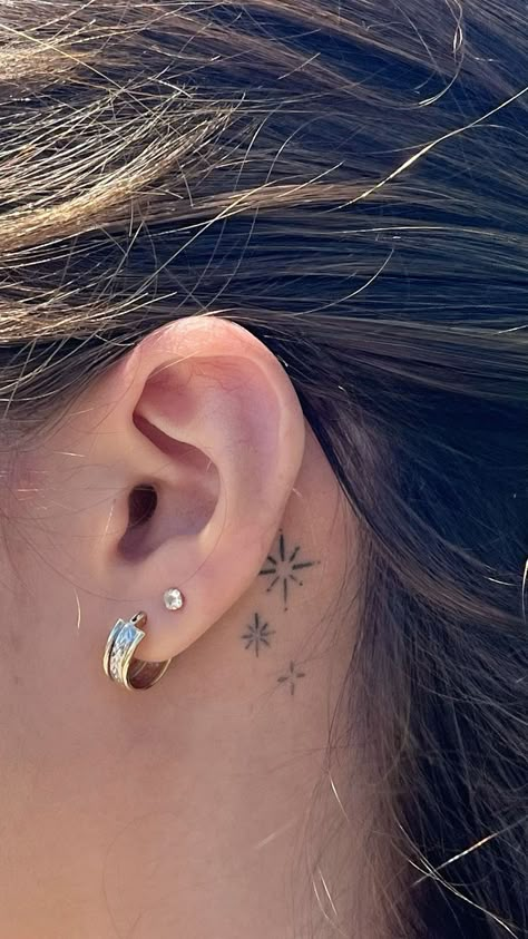 Behind-the-ear tattoos are both discreet and stylish. This hidden location is perfect for small dainty tattoos, whether you choose a star, moon, or tiny initial. The placement adds a touch of mystery, as it’s often only visible when you want it to be.  The behind-the-ear location is a great option if you’re looking for something subtle but meaningful. The small surface area ensures that the design remains delicate and understated, yet it still makes a statement when seen. Small Stars Behind Ear Tattoo, Star Tat Behind Ear, Small Star Tattoo Behind Ear, Small Tattoos Ear Ideas, 3 Hearts Behind Ear Tattoo, Being Ear Tattoo, Tattoo Star Behind Ear, Behind Ear Tattoo Fine Line, Small Moon Tattoo Behind Ear