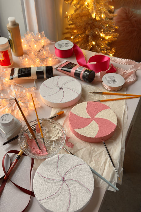 Crafts set up on a pink desk as I prep to start and oversized candy ornament DIY. Styrofoam circles are seen painted in pink and white swirls while paintbrushes, paint, ribbon, and other craft supplies are seen while the craft is in process. Sparkly christmas lights adorn the scene. Diy Pinkmas Decorations, Pink Christmas Porch Decor, Whimsy Christmas Tree, White House Decorations, Candy Wonderland Christmas Decor, Diy Whimsical Christmas Decor, Pastel Christmas Aesthetic, Oversized Decor, Pink Christmas Diy