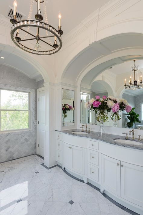 Beautiful master bathroom boasts arched alcove filled with a single wall vanity, divided into his and her sections, topped with gray marble under arched mirror flanked by medicine cabinets atop white marble tiles accented with gray marble border illuminated by ring chandelier. Arched Alcove, Bathroom Alcove, Arched Bathroom, White Marble Tile Floor, Marble Border, Bathroom Chandelier, Traditional Bathroom Designs, Sunroom Ideas, White Marble Floor