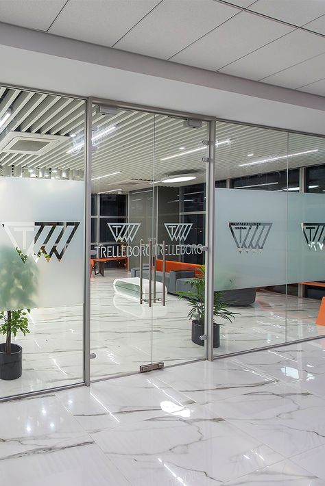 Glass Frosting can be a sure way of highlighting your branding at the workspace. When ZYETA designed the new Trelleborg's office space, the brand's logo was beautifully decorated on the glass doors, depicting brand marketing. #glassfrostingdesign #officeinteriors #workspacedesign #glassdoordecor Frosted Logo On Glass Door, Frosted Glass Office Doors, Logo Wall Design Office Branding, Glass Film Design Office Patterns, Glass Paper Design, Glass Sticker Design Office, Office Glass Design, Office Glass Door Design, Office Door Design