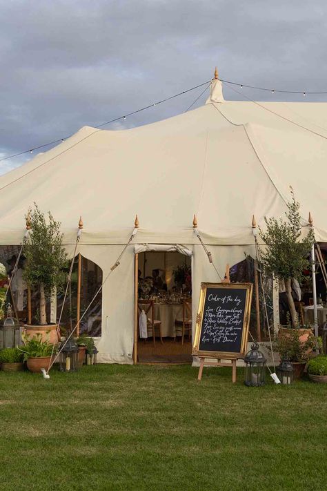 Large marquee wedding with a gold framed order of the day sign, moroccan lanterns from Onkoi and large potted plants and trees that surround the entrance of the marquee at a outdoor wedding in the Cotswolds, UK. The marquee is situated amongst a wild flower garden planted and nurtured by the bridal couple. Small Wedding Marquee, Uk Country Wedding, Wedding Flowers Marquee, Field Marquee Wedding, Garden Marquee Party, Outdoor Marquee Wedding, Backyard Wedding Marquee, Outdoor Garden Party Wedding, Wedding Marquee Flowers