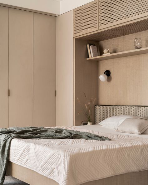 This guest bedroom exudes calm with light-toned finishes, featuring dyed oak wood veneer and beige textured laminate on wardrobes for added depth. The bed is designed to float above the floor, creating openness and maximizing space, while built-in shelves offer extra storage. Perforated shutters neatly conceal the AC unit, keeping the design sleek. A subtle green headboard adds a touch of color, complemented by custom bedside lights and built-in side tables. The paneled TV wall transitions in... Bedroom Hidden Lighting, Bed With Side Wardrobe, Wardrobe Above Bed, Paneled Tv Wall, Bed With Wardrobes Either Side, Bedroom Built Ins Around Bed, Hidden Vanity, Built In Bedroom, Bedside Wardrobe