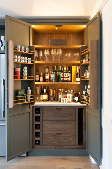 The doors of this bar cupboard open to reveal an elegantly organized space with warm walnut tones and soft interior lighting. The shelves are stocked with an array of glassware and bottles, while the door racks provide additional storage for smaller bottles and bar accessories. Below, the unit includes drawers and a dedicated section for wine storage. Cupboard Bar, Kitchen With Dark Cabinets, Bar Cupboard, Painted Shaker Kitchen, Transitional Kitchen Ideas, Transitional Kitchen Design, Clutter Free Kitchen, Kitchen Larder, Home Bar Rooms