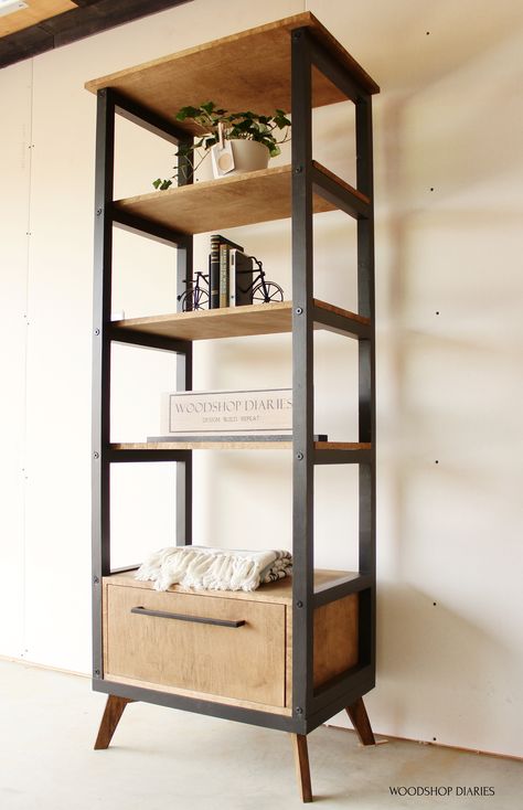 Build a two tone black and wood modern industrial bookshelf with these free building plans!! The storage drawer adds some storage to an otherwise open display bookshelf. Mid Century Modern legs add a unique touch. Made from 2x2s and plywood, this DIY bookcase is perfect for any room of the house for display and storage in one! Diy Open Bookcase, Diy Narrow Bookshelf, Diy Standing Shelf, Diy Wood Bookshelf, Unique Furniture Design Wood, Modern Industrial Bookshelf, Diy Shelving Unit, Diy Industrial Bookshelf, Metal And Wood Bookshelf