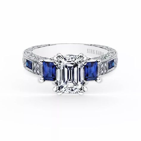 This deco inspired classic is a three stone #engagement #ring from the Charlotte collection. It features 1/10 ctw of diamonds, 2 blue sapphire baguettes, and 2 blue sapphire emeralds. The signature handcrafted details include scroll hand engravings, peek-a-boo diamonds and milgrain edging. // Kirk Kara Engangement Rings, Kirk Kara Engagement Rings, Three Stone Diamond Rings Engagement, Three Stone Engagement Ring, Buying An Engagement Ring, Three Stone Diamond, Blue Sapphire Diamond, Amber Ring, Stone Engagement Ring