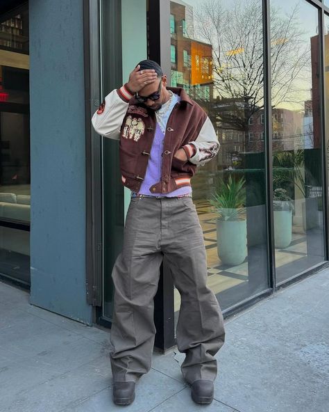 How about his color? 🍩 Outfit info 👇🏻 • • • 📸 @sylves1er 🇺🇸 🕶️Eyewear : basketcase 🧥Outer : be you 👔Top : jooniverse lab 👖Bottom : rick owens online 👞Shoes : bottega veneta • • • • • • brown varsity jacket, purple vest, gray baggy pants, boots, sunglasses, men’s outfit, usa Purple And Brown Outfit, Gray Baggy Pants, Varsity Jacket Outfit Mens, Gray Pants Outfit, Gray Shoes Outfit, Brown Varsity Jacket, Grey Pants Outfit, Outfit Info, Varsity Jacket Outfit